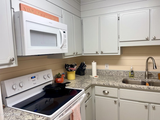 kitchen featuring white cabinetry, sink, wood walls, and white appliances