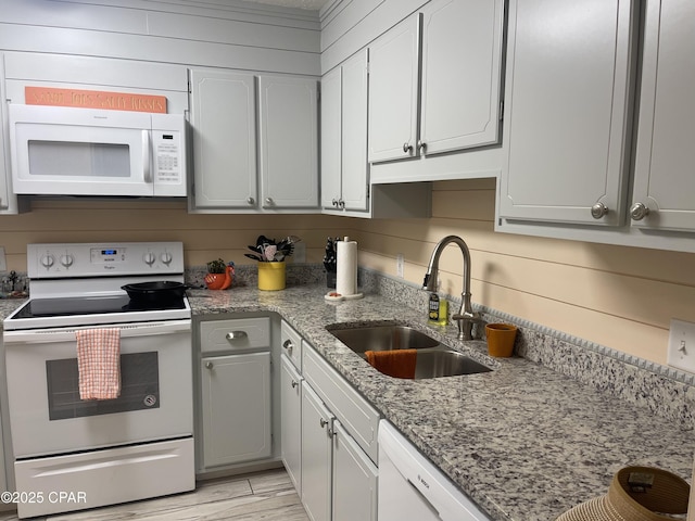 kitchen with wood walls, sink, light stone counters, and white appliances