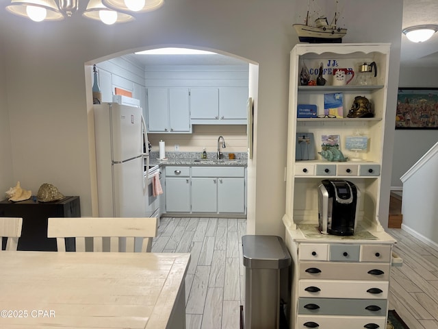 kitchen with sink, white refrigerator, light hardwood / wood-style flooring, range, and white cabinetry