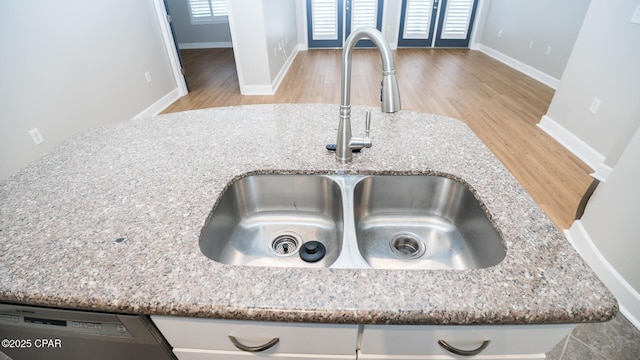 interior details featuring light stone counters, sink, stainless steel dishwasher, and light wood-type flooring