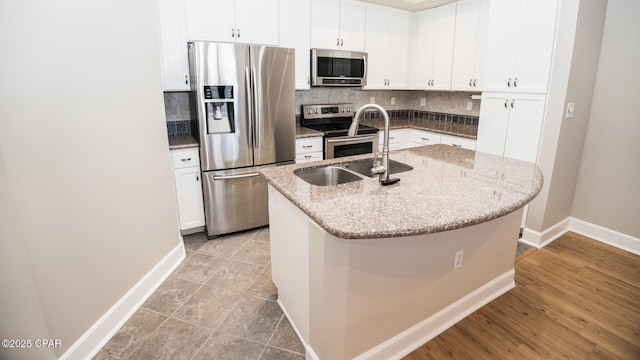 kitchen with white cabinetry, sink, stainless steel appliances, light stone counters, and a center island with sink