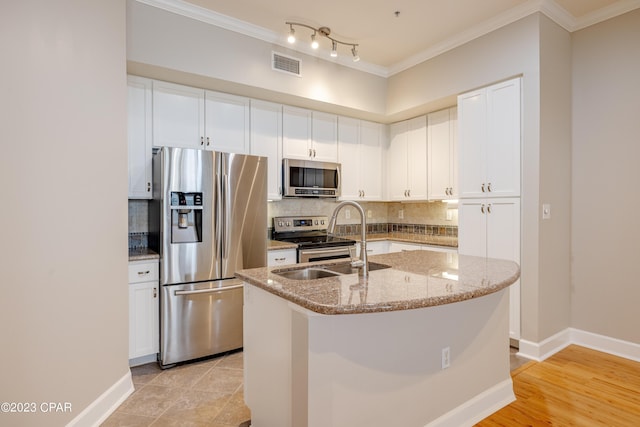 kitchen with light stone counters, stainless steel appliances, a kitchen island with sink, sink, and white cabinets