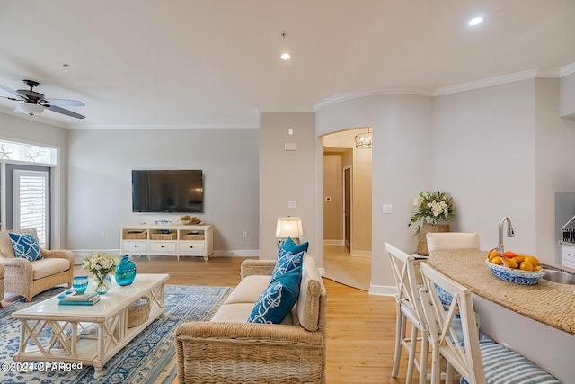 living room with ceiling fan, sink, light hardwood / wood-style floors, and ornamental molding