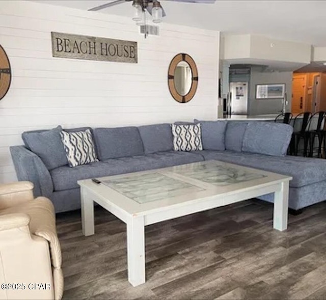 living room with hardwood / wood-style floors, ceiling fan, and wooden walls