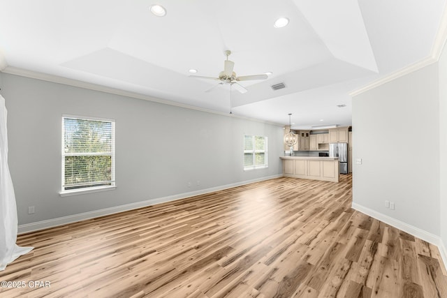 unfurnished living room with a tray ceiling, a wealth of natural light, and crown molding