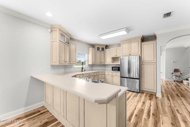 kitchen with kitchen peninsula, stainless steel appliances, crown molding, cream cabinets, and light hardwood / wood-style flooring