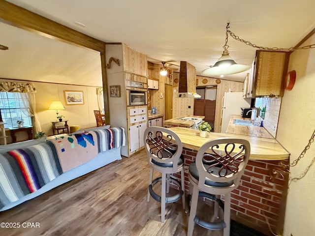 kitchen featuring sink, stainless steel microwave, wooden counters, ventilation hood, and wood-type flooring