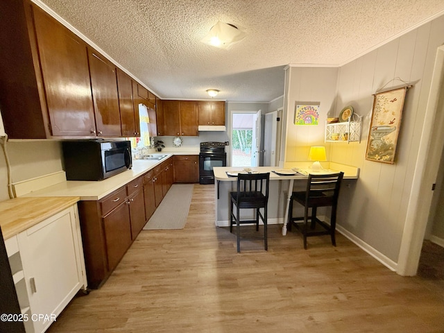 kitchen with a kitchen bar, kitchen peninsula, light hardwood / wood-style flooring, and black / electric stove