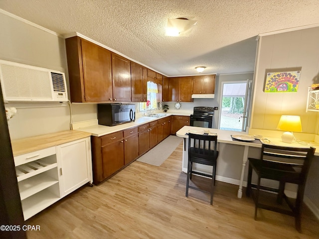 kitchen featuring sink, light hardwood / wood-style flooring, an AC wall unit, a breakfast bar area, and black appliances