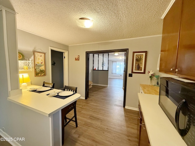 kitchen featuring a kitchen breakfast bar, kitchen peninsula, crown molding, a textured ceiling, and light wood-type flooring