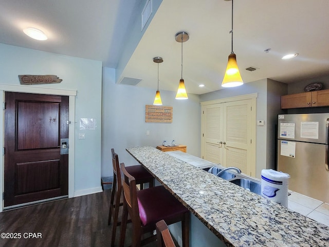 kitchen featuring a kitchen breakfast bar, light stone counters, decorative light fixtures, dark hardwood / wood-style flooring, and stainless steel refrigerator