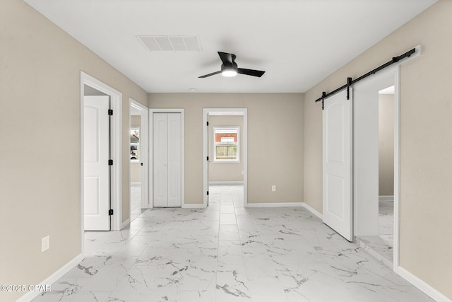 unfurnished bedroom featuring a barn door, ceiling fan, and a closet