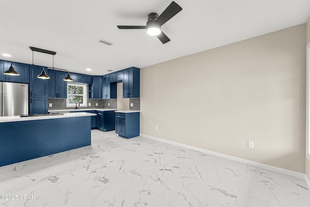 kitchen with pendant lighting, ceiling fan, stainless steel fridge, blue cabinetry, and tasteful backsplash