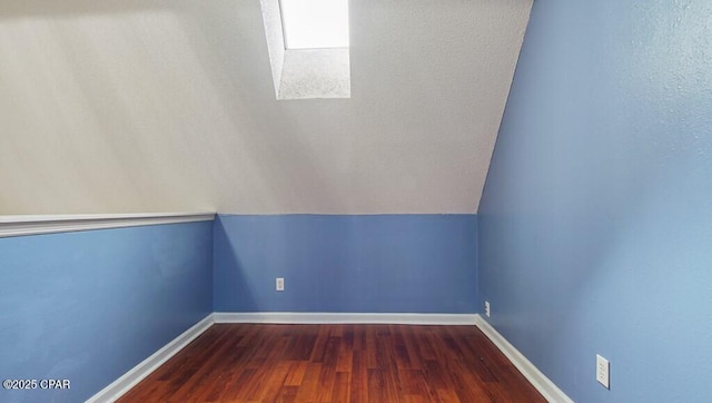 bonus room featuring lofted ceiling with skylight and dark wood-type flooring