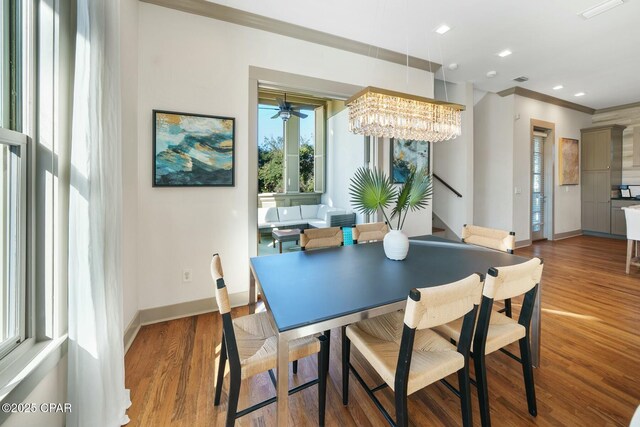 dining space with wood-type flooring, ceiling fan with notable chandelier, and ornamental molding