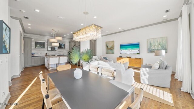 dining space with light hardwood / wood-style flooring, crown molding, and a notable chandelier