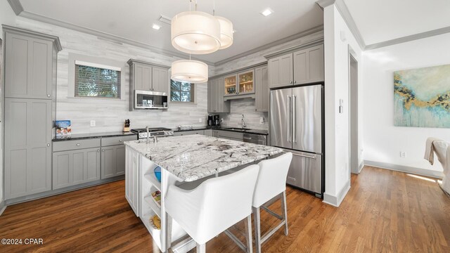 kitchen with appliances with stainless steel finishes, light stone counters, sink, pendant lighting, and a center island