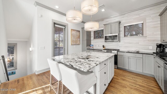 kitchen with gray cabinetry, a center island, hanging light fixtures, backsplash, and appliances with stainless steel finishes