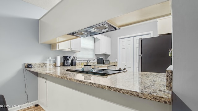 kitchen featuring light stone countertops, stainless steel fridge, black electric stovetop, white cabinets, and range hood