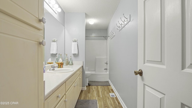 full bathroom with washtub / shower combination, a textured ceiling, toilet, vanity, and hardwood / wood-style flooring