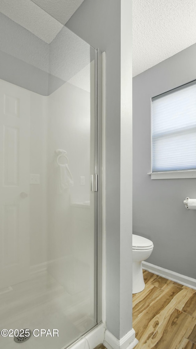 bathroom featuring a textured ceiling, hardwood / wood-style flooring, toilet, and a shower with door