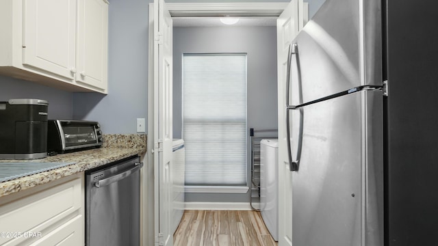 kitchen with white cabinetry, stainless steel appliances, light stone counters, light hardwood / wood-style floors, and washer / dryer