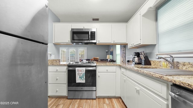 kitchen with light stone counters, stainless steel appliances, sink, white cabinets, and light hardwood / wood-style floors