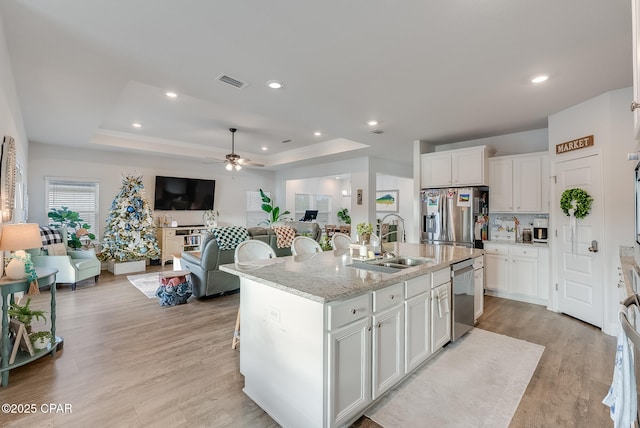 kitchen with sink, stainless steel appliances, a raised ceiling, and a center island with sink