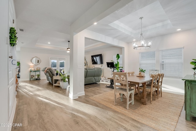 dining area featuring crown molding, a raised ceiling, ceiling fan with notable chandelier, and light hardwood / wood-style flooring