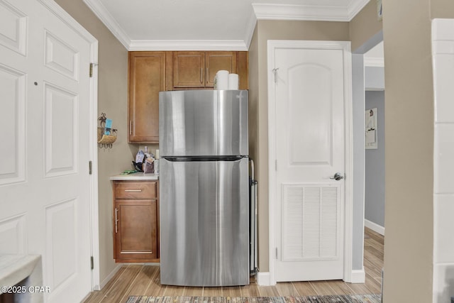 kitchen featuring crown molding, freestanding refrigerator, light wood-type flooring, and brown cabinetry
