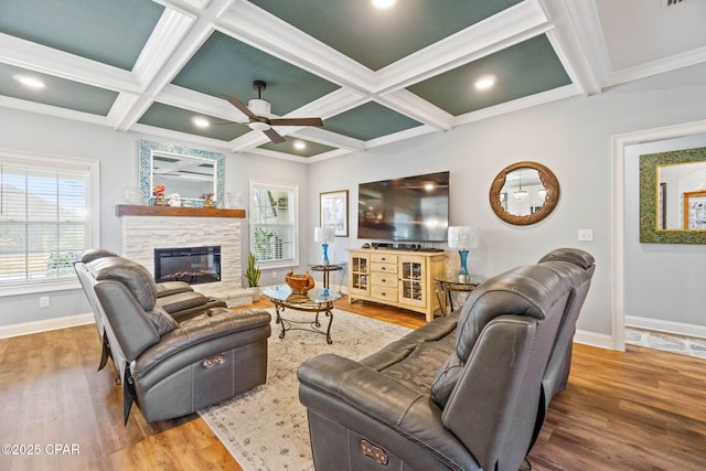 living room featuring a stone fireplace, crown molding, ceiling fan, and coffered ceiling