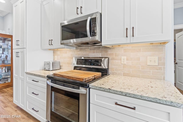 kitchen with light stone countertops, light wood-type flooring, stainless steel appliances, crown molding, and white cabinetry