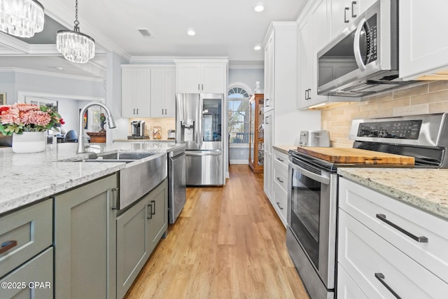 kitchen featuring pendant lighting, white cabinetry, stainless steel appliances, and ornamental molding