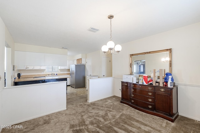 kitchen featuring stainless steel refrigerator, white cabinetry, hanging light fixtures, a notable chandelier, and light colored carpet