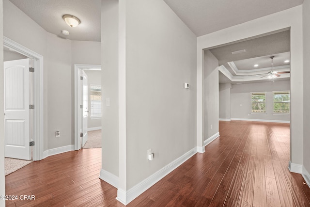 corridor with a textured ceiling, a tray ceiling, crown molding, and hardwood / wood-style floors