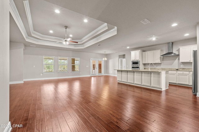 unfurnished living room featuring a raised ceiling, ornamental molding, ceiling fan, and dark wood-type flooring