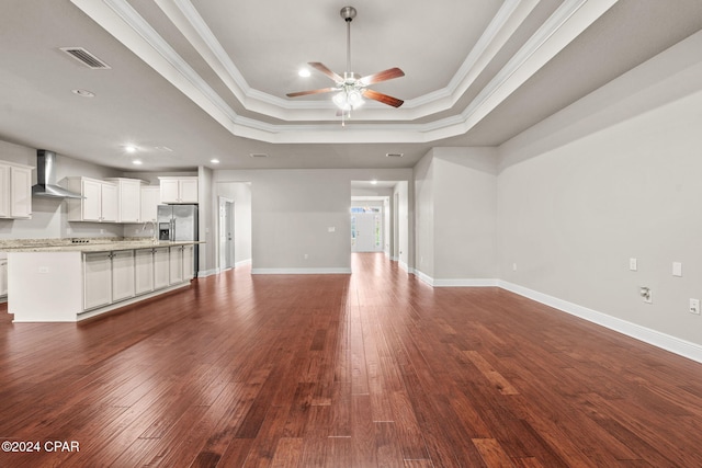 unfurnished living room featuring dark wood-type flooring, a raised ceiling, ceiling fan, and ornamental molding