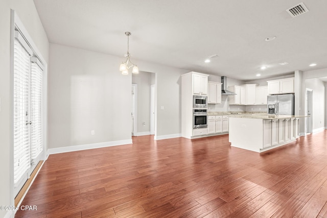 kitchen featuring appliances with stainless steel finishes, white cabinets, an island with sink, and wall chimney range hood