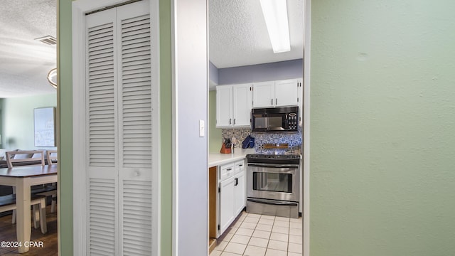 kitchen with stainless steel range with electric stovetop, black microwave, white cabinets, and light tile patterned flooring