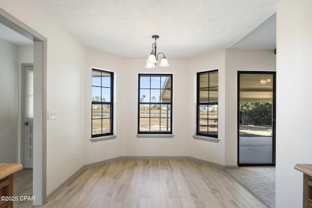 unfurnished dining area with a textured ceiling, light hardwood / wood-style floors, and a notable chandelier