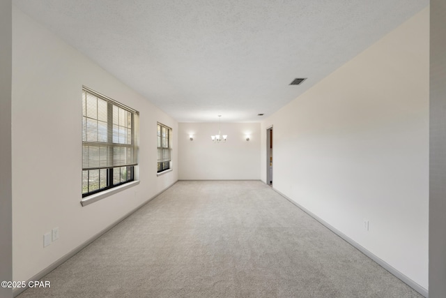 spare room featuring light colored carpet, a chandelier, and a textured ceiling