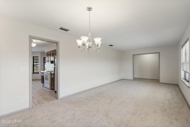 empty room featuring light colored carpet, a wealth of natural light, and a chandelier