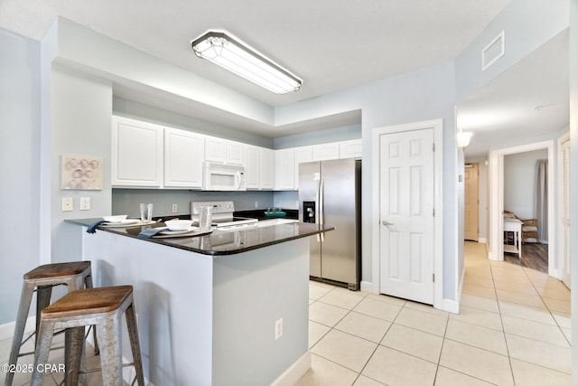 kitchen featuring a breakfast bar, white appliances, kitchen peninsula, light tile patterned floors, and white cabinetry