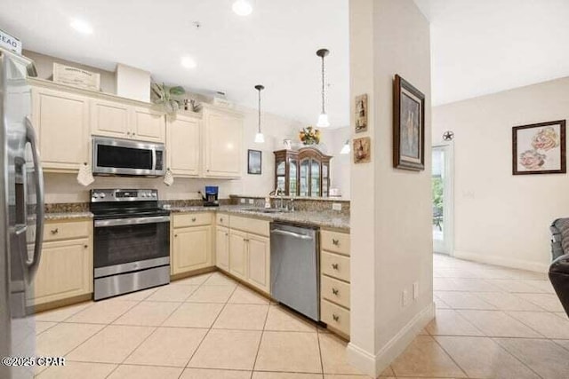 kitchen with baseboards, decorative light fixtures, light tile patterned floors, cream cabinetry, and stainless steel appliances