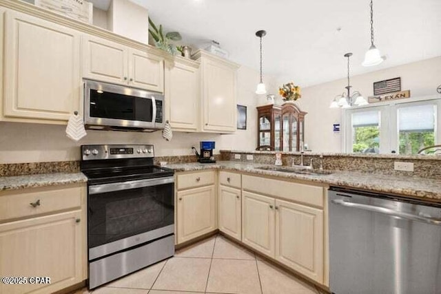 kitchen featuring cream cabinetry, a sink, stainless steel appliances, an inviting chandelier, and light tile patterned flooring