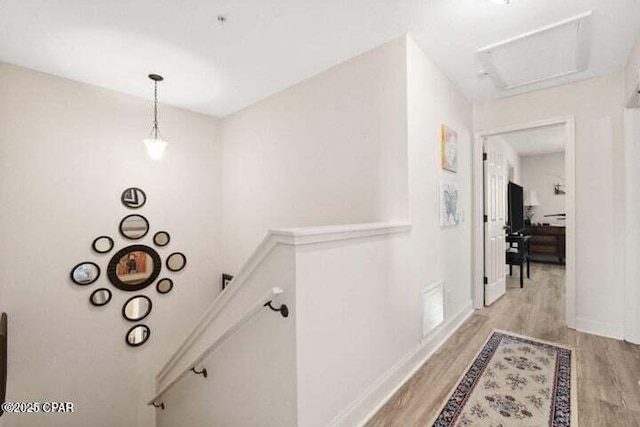 hall featuring visible vents, an upstairs landing, baseboards, and light wood finished floors