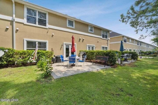 rear view of house featuring stucco siding, a lawn, and a patio