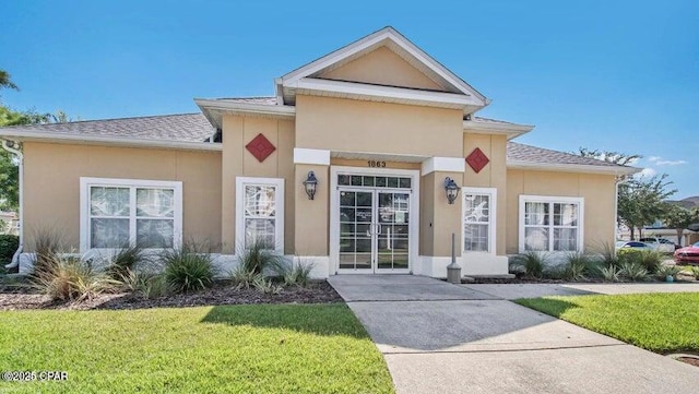 view of front of home with a front yard, roof with shingles, and stucco siding