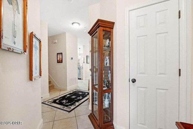 corridor featuring baseboards, light tile patterned flooring, and stairs