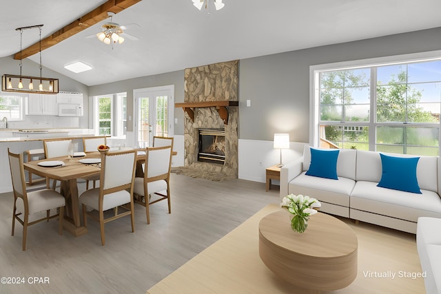 dining room featuring vaulted ceiling with beams, ceiling fan, a fireplace, and light hardwood / wood-style floors